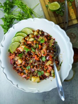 A bowl full of black chickpea, potatoes, vegetables and tamarind sauce.